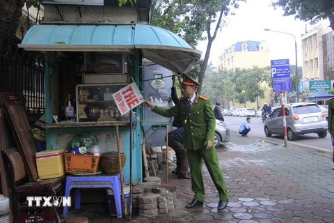 Lực lượng chức năng tiến hành tháo dỡ biển quảng cáo tại cửa hàng lấn chiếm vỉa hè trên phố Quang Trung. (Ảnh: Thùy Dương/TTXVN)