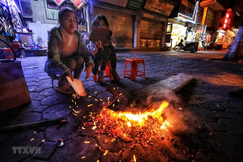 Các e nhỏ ngồi nhóm lửa sưởi ấm trên phố Nguyễn Thái Học, Hà Nội. (Ảnh: Thành Đạt/TTXVN)