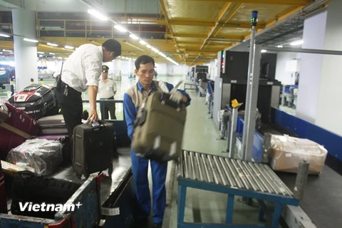 Nhân viên bốc dỡ hành lý của hành khách tại nhà ga T2 Nội Bài. (Ảnh: Việt Hùng/Vietnam+)