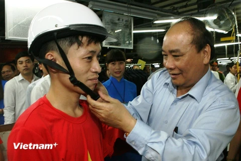 Phó Thủ tướng Chính phủ Nguyễn Xuân Phúc đội mũ bảo hiểm đạt chuẩn cho công nhân Xí nghiệp may 888. (Ảnh: Huy Hùng/Vietnam+)
