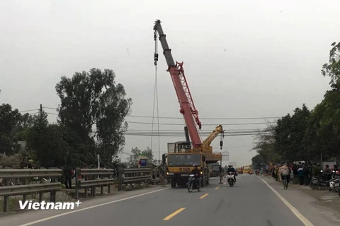 Xe cẩu đến ứng cứu kéo chiếc xe tải ra khỏi hộ lan giữa đường sắt và đường bộ. (Ảnh: PV/Vietnam+)