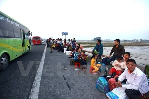 Người dân ngồi la liệt, thành hàng dài dọc đường để bắt xe khách. (Ảnh: Minh Sơn/Vietnam+)