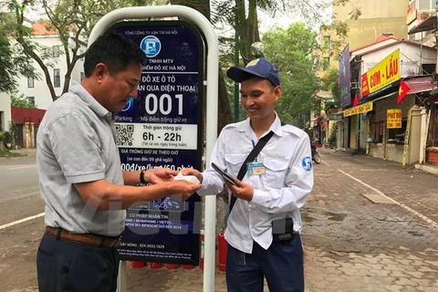 Khách hàng nhận hóa đơn từ nhân viên trông giữ phương tiện tại điểm đỗ sử dụng công nghệ iParking trên phố Lý Thường Kiệt. (Ảnh: Việt Hùng/Vietnam+)