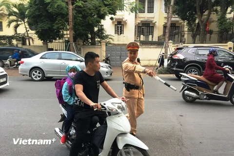 Cảnh sát giao thông phát hiện phụ huynh chở con em đều không đội mũ bảo hiểm. (Ảnh: Việt Hùng/Vietnam+)