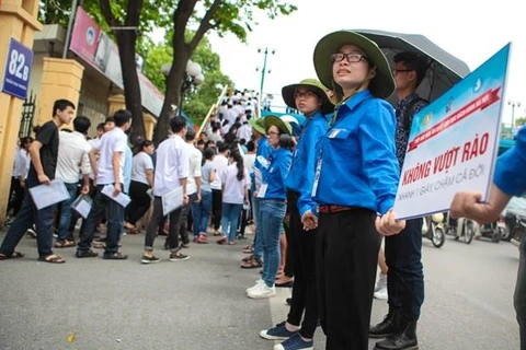 Sinh viên tình nguyện của trường Đại học Kinh tế quốc dân đứng sát nhau tạo thành hàng rào giúp các thí sinh nhanh chóng rời trường sau giờ thi. (Ảnh: Minh Sơn/Vietnam+)