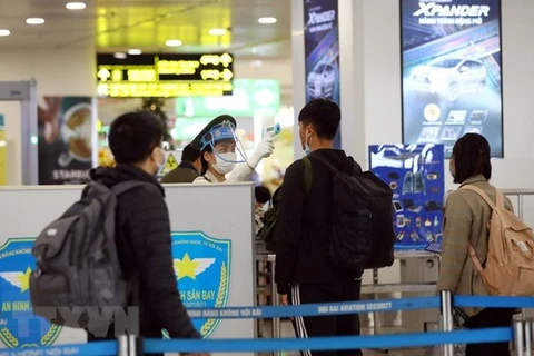 Nhân viên an ninh hàng không tại sân bay Nội Bài kiểm tra thân nhiệt của hành khách. (Ảnh: Huy Hùng/TTXVN)