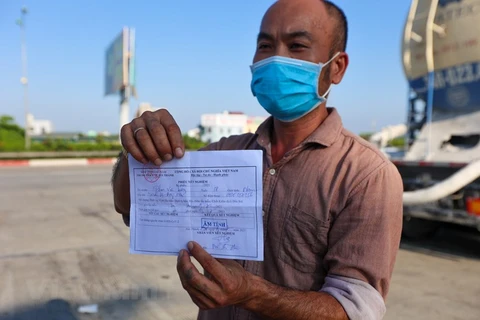 Một tài xế xuất trình giấy xét nghiệm âm tính COVID-19 để được qua chốt kiểm dịch. (Ảnh: Minh Sơn/Vietnam+)