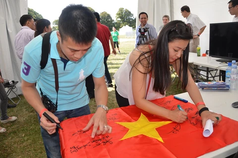 Sinh viên ký tên lên lá cờ Tổ Quốc, thể hiện tình yêu và trách nhiệm đối với quê hương đất nước. (Ảnh: Bích Hà/Vietnam+)
