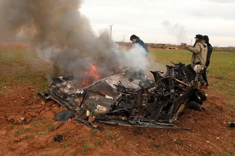 Những người có vũ trang đứng cạnh xác một chiếc trực thăng của quân đội Syria bị bắn hạ tại làng Qaminas. (Nguồn: EPA)