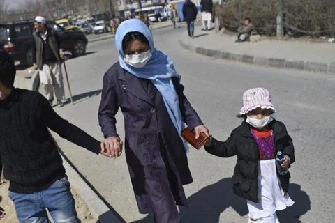 Một phụ nữ dắt hai con nhỏ đeo khẩu trang chống COVID-19 đi bộ dọc theo một con đường ở Kabul ngày 18/3. (Nguồn: AFP)