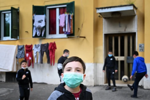 Trẻ em đeo khẩu trang khi chơi trước cửa nhà ở San Basilio, Rome, Italy ngày 18/4/2020 trong bối cảnh dịch COVID-19 đang hoành hành. (Ảnh: AFP/TTXVN)
