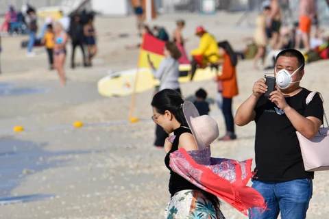 Khách du lịch đeo khẩu trang vui chơi trên bãi biển Dubai, UAE. (Ảnh: AFP/TTXVN)