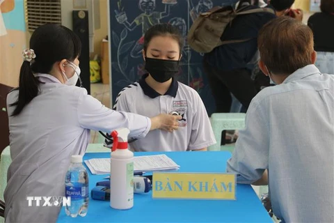 Nhân viên y tế khám sàng lọc cho học sinh tại điểm tiêm vaccine COVID-19 trường Tiểu học Nguyễn Bỉnh Khiêm (quận 1). (Ảnh: Thu Hương/TTXVN)