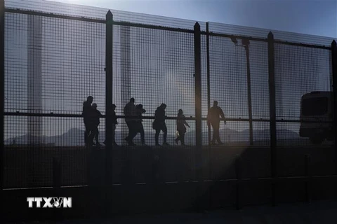 Lực lượng bảo vệ biên giới Mỹ (trái) bắt giữ người di cư trái phép tại biên giới Mexico - Mỹ, ở El Paso, Texas, ngày 21/12/2022. (Ảnh: AFP/TTXVN)