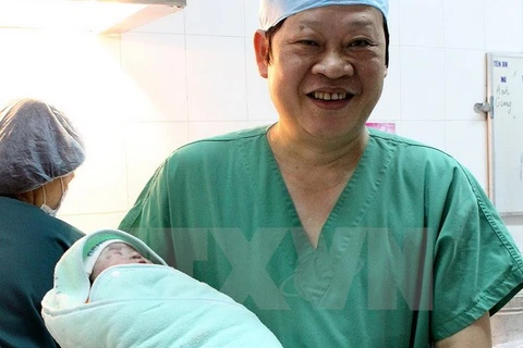 Giáo sư, tiến sỹ Nguyễn Viết Tiến, Thứ trưởng Bộ Y tế - người trực tiếp thực hiện phẫu thuật lấy thai cho ca mang thai hộ đầu tiên tại Bệnh viện Phụ sản Trung ương - bế bé gái mới sinh. (Ảnh: Dương Ngọc/TTXVN)