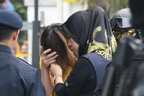 Nghi phạm Đoàn Thị Hương (áo vàng) che mặt khi bị cảnh sát áp giải tới phiên tòa. (Ảnh: AFP)