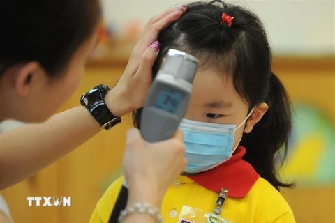 Kiểm tra thân nhiệt cho trẻ em tại một trường mầm non ở Hong Kong, Trung Quốc, để ngăn ngừa sự lây lan của dịch cúm. (Ảnh: AFP/TTXVN)
