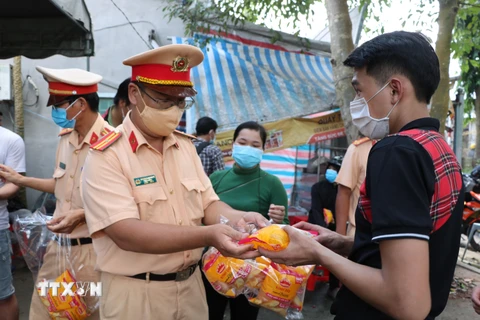 Cảnh sát giao thông Công an tỉnh Bến Tre hỗ trợ thức ăn, nước uống cho người dân làm thủ tục tại chốt cầu Rạch Miễu. (Ảnh: Huỳnh Phúc Hậu/TTXVN)