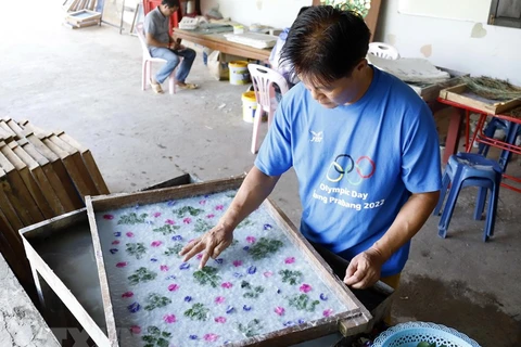 Nghệ nhân Nalongkone Khounphachansi, chủ cơ sở làm giấy Saa tại bản Xienglek, tỉnh Luang Prabang, trang trí hoa lá lên khuôn giấy. (Ảnh: Phạm Kiên/TTXVN) 