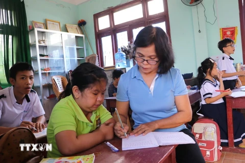 Cô giáo Nguyễn Thị Hương, xã Hành Minh, huyện Nghĩa Hành, hướng dẫn học sinh viết bài.( Ảnh: Đinh Hương/ TTXVN)