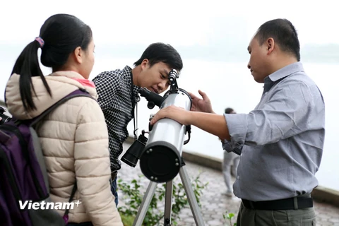 Anh Đặng Vũ Tuấn Sơn (phải) hướng dẫn các bạn trẻ quan sát bầu trời qua kính thiên văn. (Ảnh: Doãn Đức/Vietnam+)