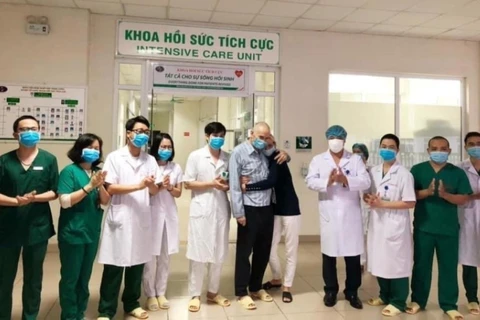 Vợ chồng ông Dixong (mặc áo bệnh nhân/áo đen) và các nhân viên y tế Bệnh viện Bệnh nhiệt đới Trung ương đêm 13/4. (Ảnh: PV/Vietnam+)