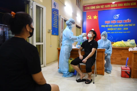 Nhân viên y tế quận Ba Đình lấy mẫu xét nghiệm cho các tiểu thương khu hải sản chợ Long Biên. (Ảnh: Thành Đạt/TTXVN)