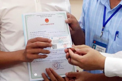 Lãnh đạo bảo hiểm xã hội trao giấy khai sinh và thẻ bảo hiểm y tế theo dịch vụ công liên thông. (Ảnh: PV/Vietnam+)