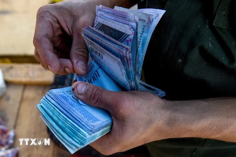Người dân đếm tiền mệnh giá 1.000 Bolivar của Venezuela để mua hàng hóa tại một khu chợ ở Coche. (Nguồn: AFP/TTXVN)