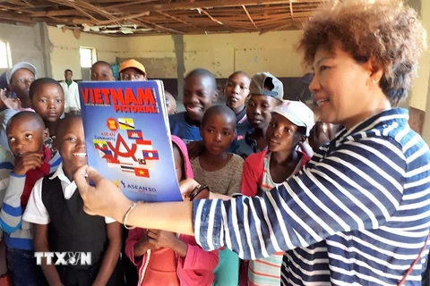 Phu nhân Đại sứ Việt Nam tại Nam Phi Trịnh Minh Hằng giới thiệu Báo Ảnh Việt Nam của TTXVN với trẻ em Lesotho. (Ảnh: Phi Hùng/TTXVN)