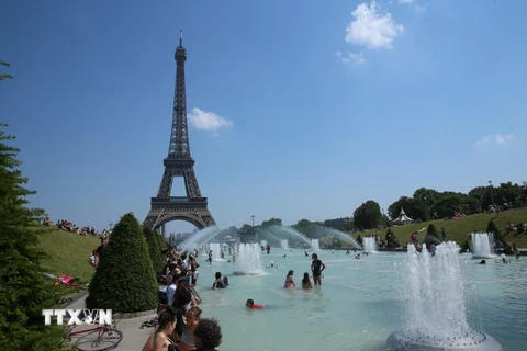 Người dân tránh nắng nóng bên vòi phun nước ở Paris, Pháp. (Nguồn: THX/TTXVN)