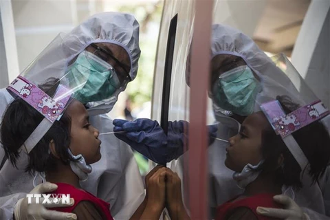 Nhân viên y tế lấy mẫu dịch xét nghiệm COVID-19 cho trẻ em tại Surabaya, Indonesia. (Ảnh: AFP/TTXVN)