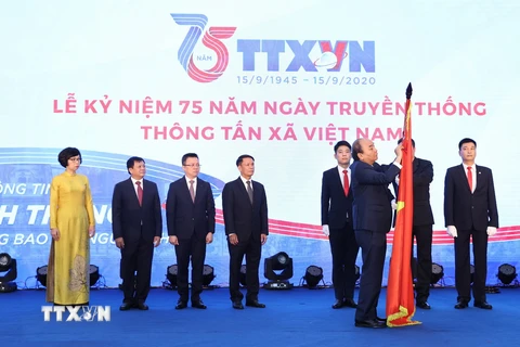 Thủ tướng Nguyễn Xuân Phúc gắn Huân chương Lao động hạng Nhất lên lá cờ truyền thống của Thông tấn xã Việt Nam. (Ảnh: Thống Nhất/TTXVN)