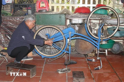 Ông Lê Trọng Kính sửa xe đạp cũ để tặng học sinh nghèo. (Ảnh: Thùy Dung/TTXVN)