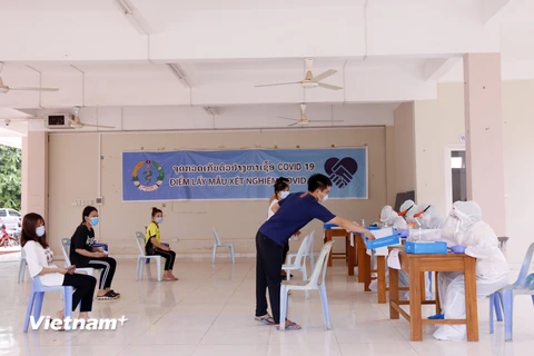 Các sinh viên Việt Nam nộp giấy khai tên họ, số điện thoại và khai lịch sử đi lại cho các nhân viên y tế Lào trước khi lấy mẫu xét nghiệm. (Ảnh: Phạm Kiên/Vietnam+)