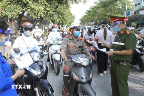 Lực lượng chức năng kiểm tra giấy tờ tùy thân và xác nhận đi làm, ra ngoài của cơ quan với người dân lưu thông trên đường Đào Tấn, Hà Nội, sáng 28/7. (Ảnh: Lâm Khánh/TTXVN)