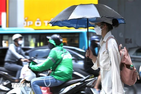 Người dân sử dụng ô, quần áo chống nóng khi phải di chuyển ngoài trời. (Ảnh: Hoàng Hiếu/TTXVN)