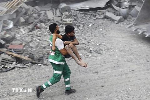 Lực lượng dân phòng Palestine chuyển một em nhỏ bị thương sau cuộc không kích của Israel xuống thành phố Gaza. (Ảnh: AFP/TTXVN)
