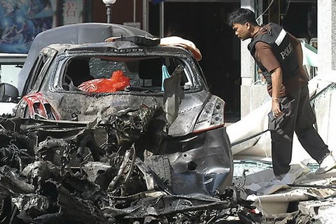 Một cảnh sát Thái Lan nhìn vào đống đổ nát của một chiếc xe máy và một chiếc xe ôtô sau một vụ nổ bên ngoài một khách sạn ở huyện Sadao, tỉnh Songkhla, miền nam Thái Lan. (Nguồn: AP)