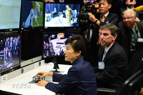 Tổng thống Hàn Quốc Park Geun-hye (giữa) điều khiển một cánh tay robot trong chuyến thăm Trung tâm Goddard. (Ảnh: Yonhap/TTXVN)