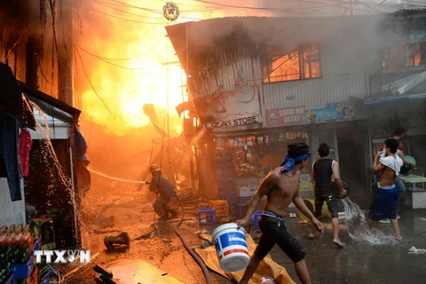 Nhân viên cứu hỏa và người dân địa phương nỗ lực khống chế một đám cháy tại khu dân cư nghèo ở khu vực ngoại ô thủ đô Manila. (Ảnh: AFP/TTXVN)