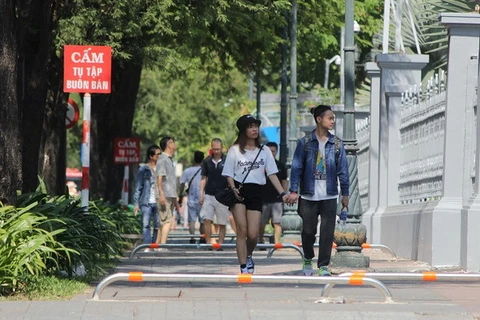 Du khách đi bộ trên vỉa hè vừa lắp các thanh barie tuyến đường Lý Tự Trọng. (Ảnh: Hoàng Hải/TTXVN)
