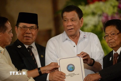 Tổng thống Rodrigo Duterte (giữa) và đại diện của MILF giơ cao dự luật mang tên “Luật Cơ bản Bangsamoro” tại buổi lễ ở Manila. (Ảnh: AFP/TTXVN) 