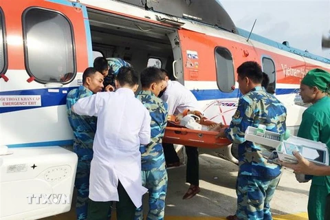 Các y bác sỹ Bệnh viện Quân y 175 cùng cán bộ, chiến sỹ, quân y đảo Phan Vinh đưa hai bệnh nhân lên máy bay. (Ảnh: TTXVN)