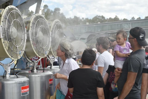 Người dân tránh nóng bằng quạt hơi nước tại Sydney. (Ảnh: AFP/TTXVN)