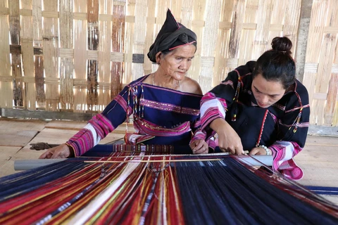 Chị Hồ Thị Viên (bên phải) cùng một nghệ nhân lớn tuổi hoàn thành sản phẩm thổ cẩm tại làng dệt Pơ Nang, xã Tú An, thị xã An Khê, tỉnh Gia Lai. (Ảnh: Hồng Điệp/TTXVN)