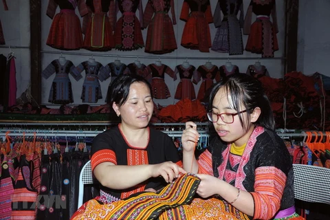 Chị Tráng Thị Dua (bên trái) truyền dạy nghề thêu, may truyền thống của đồng bào dân tộc Mông cho con gái. (Ảnh: Quang Quyết/TTXVN)