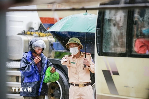 Lực lượng chức năng làm nhiệm vụ dưới mưa, hướng dẫn công dân thực hiện các quy định khi lưu thông qua chốt. (Ảnh: Trọng Đạt/TTXVN)