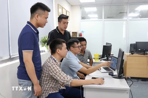 Anh Vũ Văn Hạnh (ngồi ở giữa) trao đổi với các đồng nghiệp về ứng dụng Phản ánh kiến nghị trên thiết bị di động. (Ảnh: Thanh Thương/TTXVN)