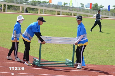 Tình nguyện viên hỗ trợ bố trí dụng cụ rào chắn vào sân thi đấu môn chạy vượt rào. (Ảnh: Văn Dũng/TTXVN)